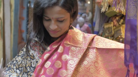 An attractive happy woman interacting or talking with the shopkeeper and choosing from the various ethnic sarees or traditional clothes displayed at the shop during the festival 