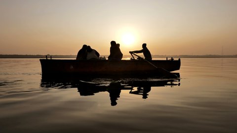 A Silhouette beautiful shot of a man rowing a boat and taking the tourists for a wooden boat ride in the South Asian river 