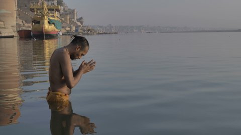 A Hindu priest or pandit standing in the water on the banks of the Ganges, bowing before the Sun in the morning and offering Suryanamaskar, and praying to the morning sun on the banks of  Varanasi.
