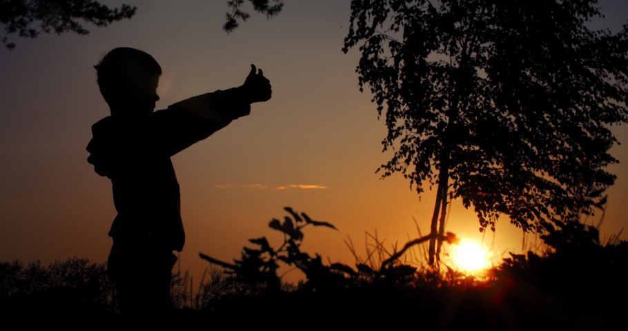 Boy shows class, thumbs up silhouette shot against the backdrop of the setting sun.