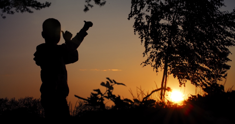 Boy shows class, thumbs up silhouette shot against the backdrop of the setting sun.