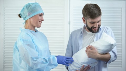 Smiling nurse giving young happy father newborn child, miracle of birth, care