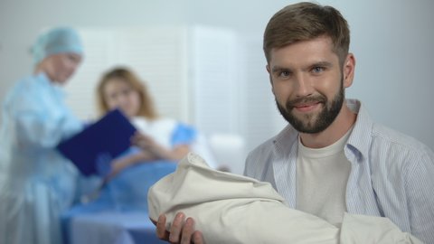 Happy father holding newborn child during nurse explaining wife postnatal care