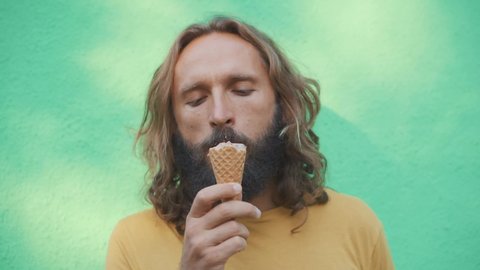 Bearded man in yellow t-shirt and black sunglasses eating chocolat ice cream in waffle cone. Urban city life Way to cool in the heat. Dessert tasting. Appetizingly bites. Close up ice cream on beard. 