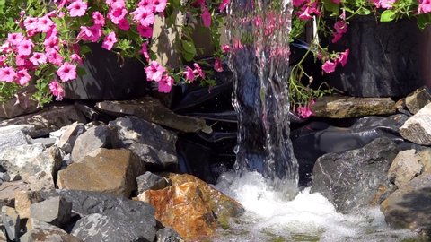 Beautiful landscaping. Man-made small waterfall on the background of petunia flowers.