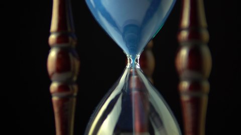Rotating hourglass clock time concept. Old vintage wood frame blue sand clock slowly spinning on dark background. Close up.
