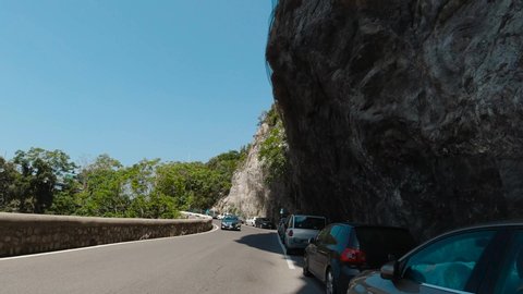 Positano, Italy, August 2019: POV dash camera tracking shot front view of driving in traffic of the mountainous curvy narrow road of Amalfi coast getting close to Positano town in Italy