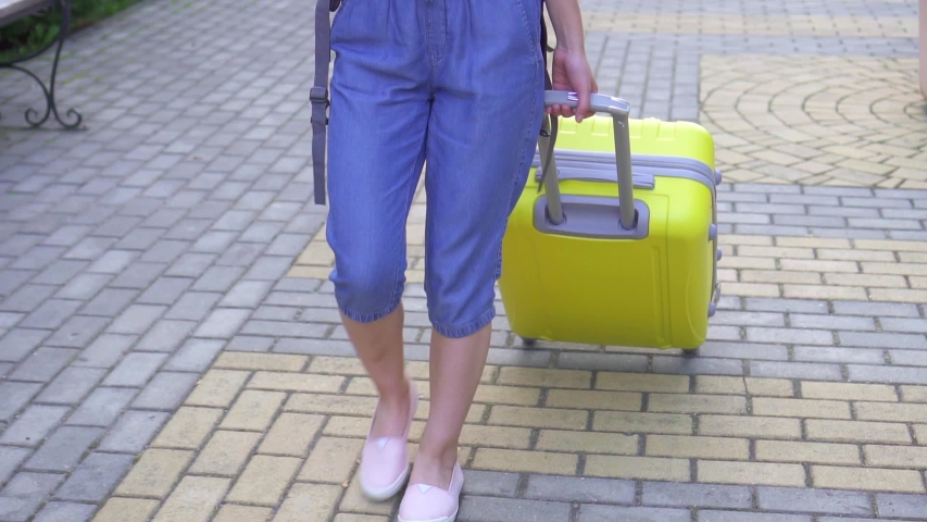 Positive young woman tourist asian appearance with a suitcase and a smartphone in his hand is in the park slow mo