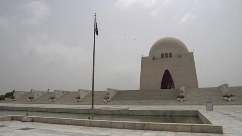 Karachi Mazar-e-Quaid Jinnah Mausoleum Frontal View with Pond and Waving Pakistan Flag on a Cloudy Day