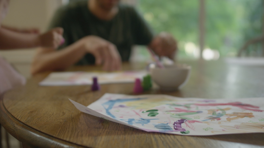 Cute little blonde girl in a pink tutu, plays with paints and stamps with her daddy at the kitchen table