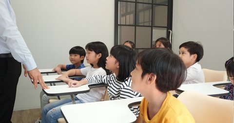 Asian teacher teaching children in the classroom at school. Little boy and girl raise hands together for accepting comments. Concept of education, experience learning and skill development.