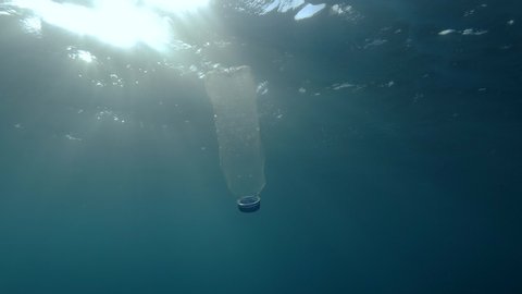 Plastic pollution, plastic bottle in blue water. Discarded plastic bottle slowly drifting under surface of blue water in sunlight. Plastic garbage environmental pollution problem in Mediterranean Sea.