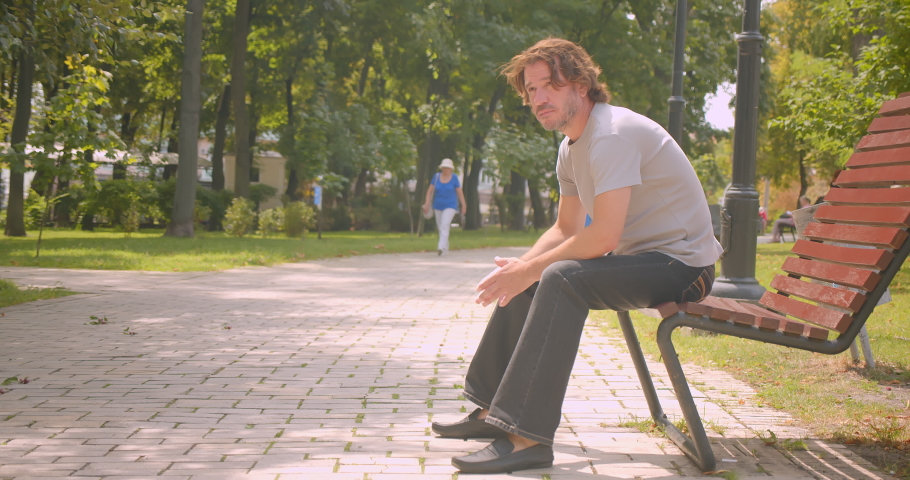 Closeup portrait of attractive caucasian man sitting on bench in park outdoors