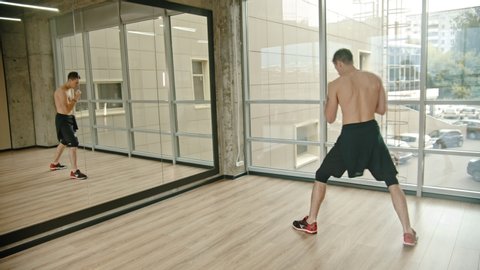 An athletic man standing in the studio - training in front of the mirror - boxing