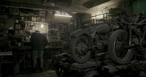 Metalworker working on a grinder with flying fiery sparks in a workshop with rows of stored vintage motorbikes in dim light