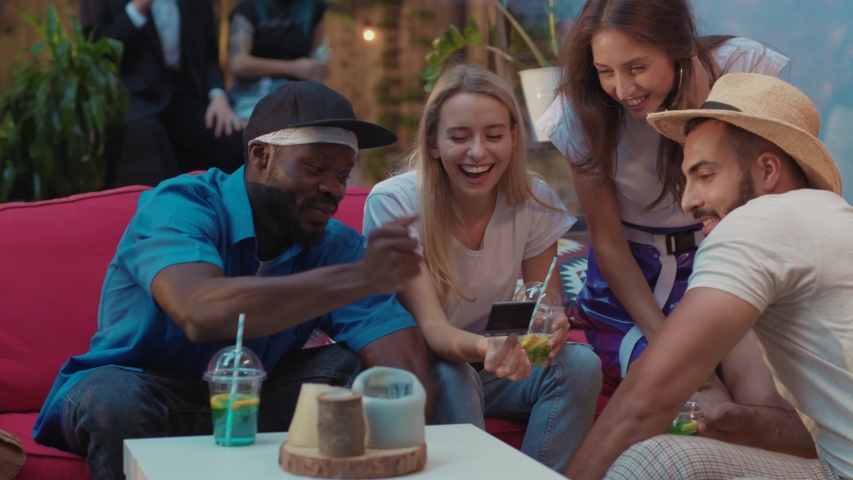 Happy friends taking group pictures looking on fresh instant polaroid photo and laughing of funny faces resting on coach at party. | Shutterstock HD Video #1036041029