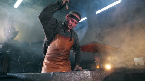 Male forger is striking metal with a hammer in slow motion