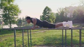 Muscular, concentrated afro guy with dark hair doing triceps dips on parallel bars with green nature around. Concept of sport, fitness and healthy lifestyle
