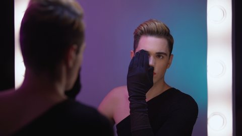 Transgender person looking at half-face makeup in mirror, accepting female inner self