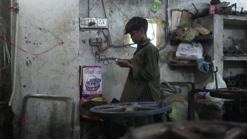 Karachi, Pakistan - 2017: A poor child worker puts a cell phone on charge before he begins his daily work in a small metal factory. 