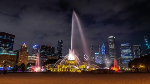 Chicago, IL - August 11th, 2019: Buckingham Fountain sprays water high in the air in front of the setting sun between the skyscrapers in Grant Park as tourists and visitors pass by.