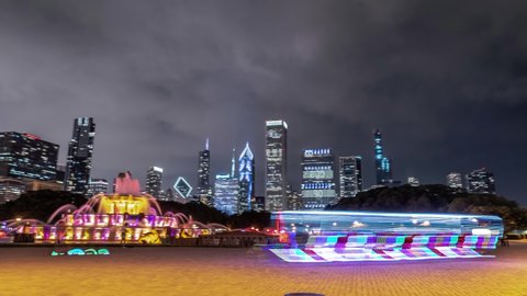 Chicago, IL - August 11th, 2019: Buckingham Fountain lights change colors as tourists and locals pass by and enjoy the display on a warm summer night as clouds pass over the skyline beyond.