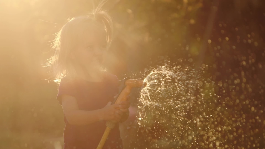 girl with pigtail silhouette sprays water to camera with garden hose at back sunlight different angle shots slow motion