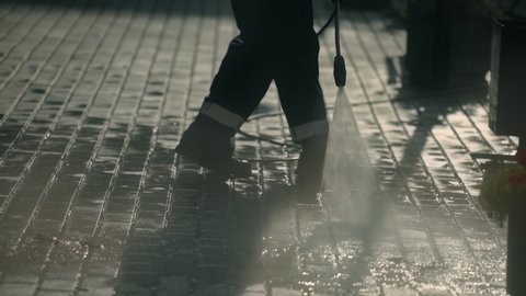People are clearing dirt from city road summer morning 4K. City worker clean sidewalk with brick block closeup hosing with powerful jet water. man in working form washes asphalt hosing cleaning agent.
