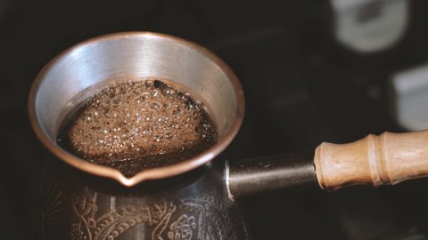 Making turkish coffee in copper cezve over gas stove. Milling of grains. On the gas stove Turk with a running coffee. Running coffee close up. gas stove with burning fire. A cup of coffee