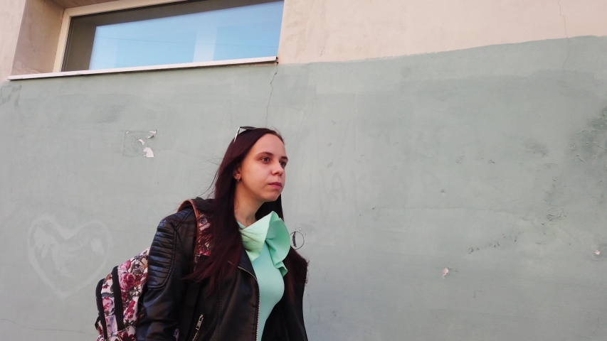 A young woman with natural beauty in a dress and leather jacket is walking down the street.