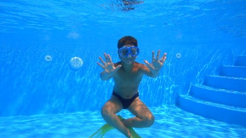 Boy dive in swimming pool and make greeting gesture, underwater slow motion