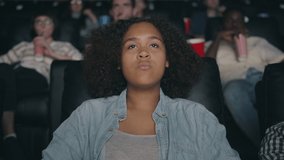 Sad African American girl is watching drama in cinema with sadness and compassion looking at screen sitting in comfy seat with friends multi-ethic group.
