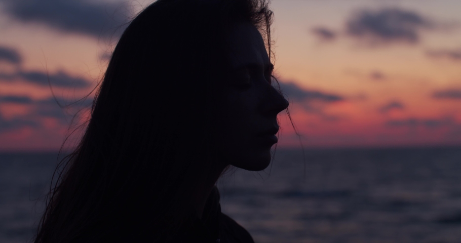 Close up side portrait of backlit girl with closed eyes dreaming at seaside in natural evening light. Young woman relaxing meditating alone on sea beach at colorful sky background. Stress overcome
 Royalty-Free Stock Footage #1036098590