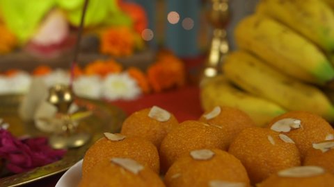 Close shot of a decorated temple for Ganesh Chaturthi - Modak, Lamp, Sweets, and Fruits. Pan shot of various items kept for worshipping Lord Ganesh in the temple - Puja thali, sweets, incense stick.