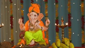 Overhead shot of an Indian female garlanding Lord Ganesha idol and praying on Ganesh Chaturthi . A young female is putting marigold garland on Ganesh Ji and praying with folded hands - Decorated fe...