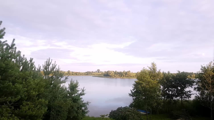 Lake Timelapse. Timelapse Of A Peaceful Lake And Mooving Clouds. Evening Sky And Coluds Over A Lake Surrounded By Trees.