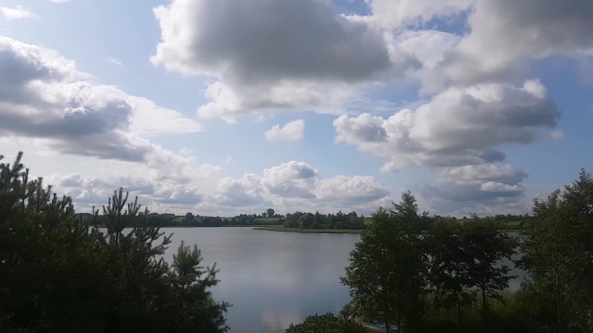 Lake Timelapse. Timelapse Of A Peaceful Lake And Mooving Clouds. Blue Sky And White Coluds Over A Lake Surrounded By Trees.