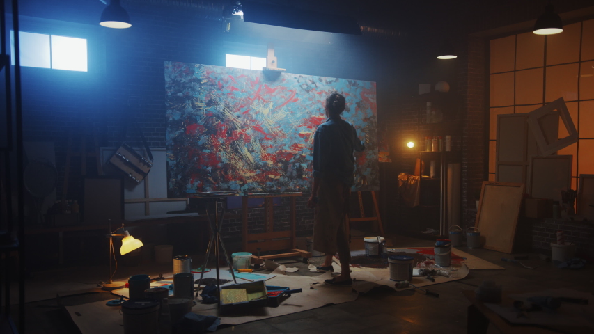 Talented Female Artist Works on Abstract Oil Painting, Using Paint Brush She Creates Modern Masterpiece. Dark and Messy Creative Studio where Large Canvas Stands on Easel Illuminated. Zoom out Royalty-Free Stock Footage #1036107545