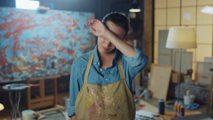 Beautiful Female Artist Dirty with Paint, Wearing Apron, Wipes Sweat from Forehead, Crosses Arms while Holding Brushes, Satisfied She Looks at Camera with a Smile. Authentic Creative Studio Royalty-Free Stock Footage #1036107650