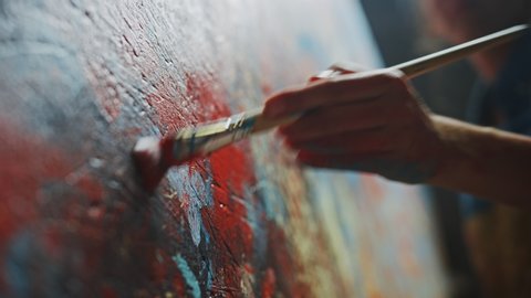 Close-up Shot of Artist Hand, Holding Paint Brush and Drawing Painting with Red Paint. Colorful, Emotional Oil Painting. Contemporary Painter Creating Modern Abstract Piece of Art