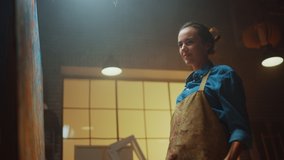 Portrait of Talented Female Artist Working on a Modern Abstract Oil Painting, Gesturing with Broad Strokes Using Paint Brush. Dark Creative Studio Large Picture Stands on Easel Illuminated. Low Angle - Powered by Shutterstock - Get 15% off with code: PIKWIZARD15