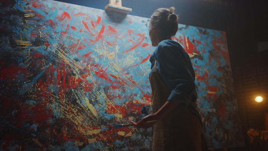 Talented Female Artist Energetically Using Paint Brush, She Creates Modern Masterpiece of the Oil Painting. Creative Studio where Large Canvas Stands on Easel Illuminated. Low Angle Following Shot Royalty-Free Stock Footage #1036107815