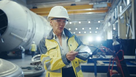 Professional Heavy Industry Female Engineer Wearing Hardhat, Holds Digital Tablet Computer and Explains Product Design for Video Conference Call. Background Industrial Factory, Pipeline Facility