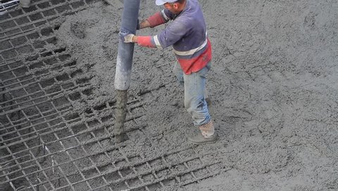 Workers working on construction site, a laborer pulling the hose for concreting. Pouring concrete mix from cement mixer on concreting formwork

