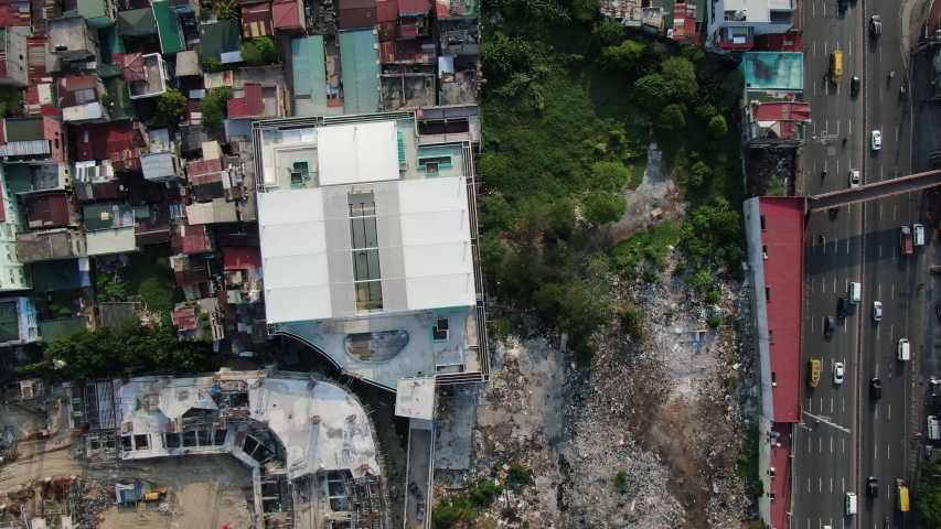 Top down view from of a rooftop of a white building surrounded by small houses at the left and a roadside in the right area.