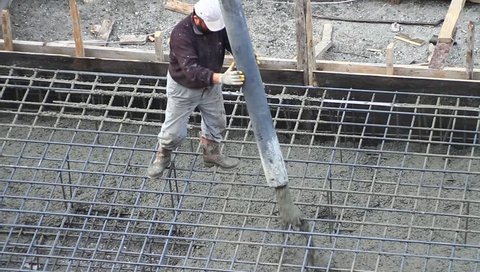 Worker pulling a large hose for concreting of steel reinforced concrete. Construction worker during concrete pouring work at the construction site.
