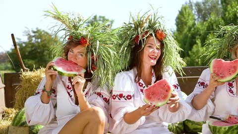 Women in ethnic costumes eating watermelons outside