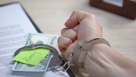 Male hand in cuffs and dollars with alimony sign on table, obligatory payment