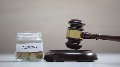 Alimony glass jar with coins on table, gavel striking on sound block, government