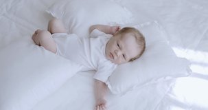 Cute newborn baby laying on white pillow on bed enjoying sun. RAW Graded footage 4K slow motion 50fps